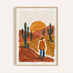 Framed desert wall art of a figure in orange jacket and cactus in earthy tones