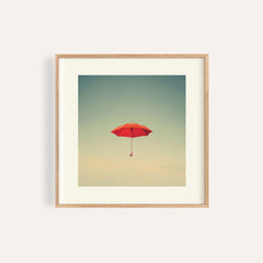 Framed print of a red umbrella floating in a minimalist cloudy sky with pale colours