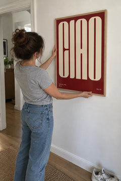Woman hanging the Ciao Rosso print in a framed oak frame in her hallway