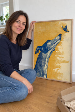 Woman sitting on the floor beside the Greyhound Butterfly print, just unboxed
