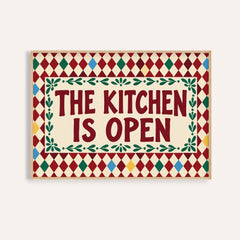 Open kitchen harlequin print reading THE KITCHEN IS OPEN on a burgundy harlequin pattern