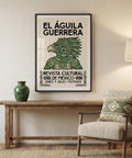 Framed artwork with 'El Águila Guerrera' on a wall above a wooden table with a vase and chair.