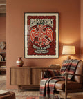 Framed poster titled 'El Maestro' on a wall above a wooden cabinet and leather chair with a patterned blanket.