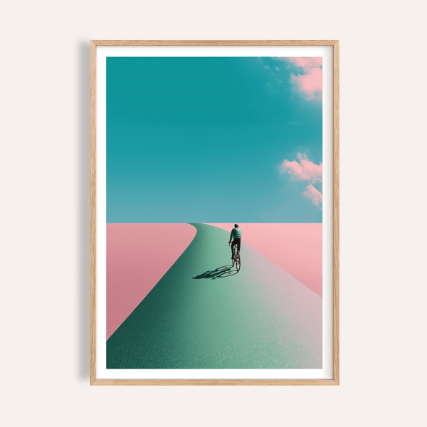 Framed mockup of Surreal Cycling Art Print poster with lone cyclist on a curved road under clouds