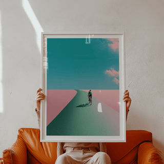 Minimal wall art print depicting a single cyclist riding toward the horizon with wide sky and clouds