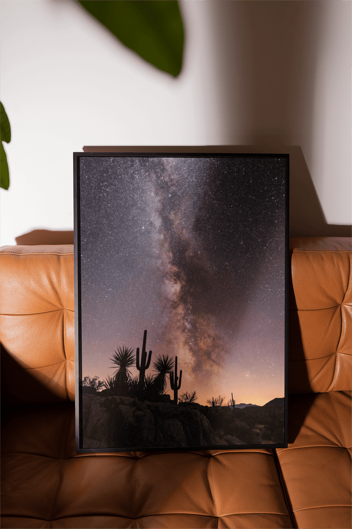 Framed Cactus Night Print of a starry sky with saguaro cacti resting on a brown leather seat