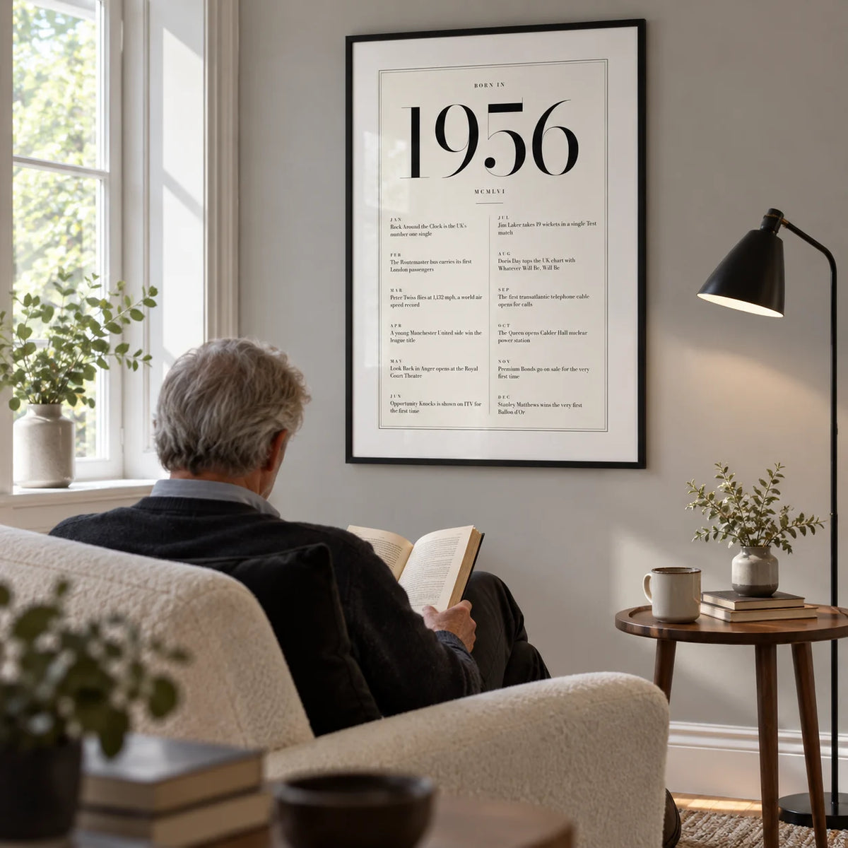 1956 Birthday Print, framed on the wall of a comfortable reading corner in a mature couple's UK home with a pale grey wall and a tall window in a living room