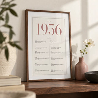 1956 Pink Birthday Print, a small A4 framed print leaning on a walnut shelf in a living room
