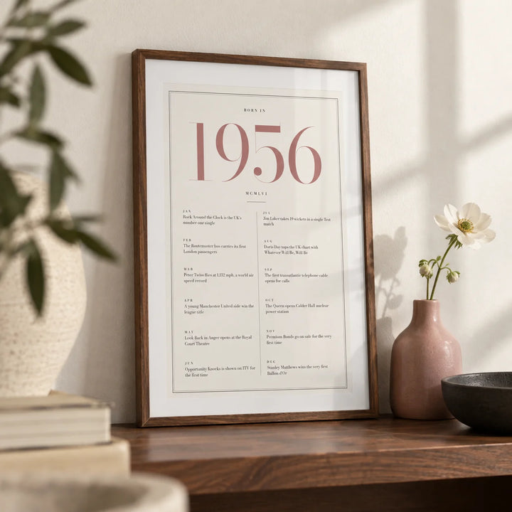1956 Pink Birthday Print, a small A4 framed print leaning on a walnut shelf in a living room