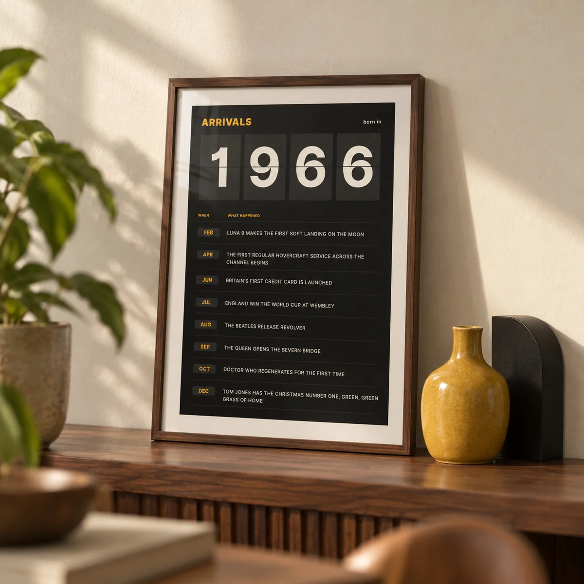 1966 Arrivals Board Print, a small A4 framed print leaning on a walnut shelf in a living room