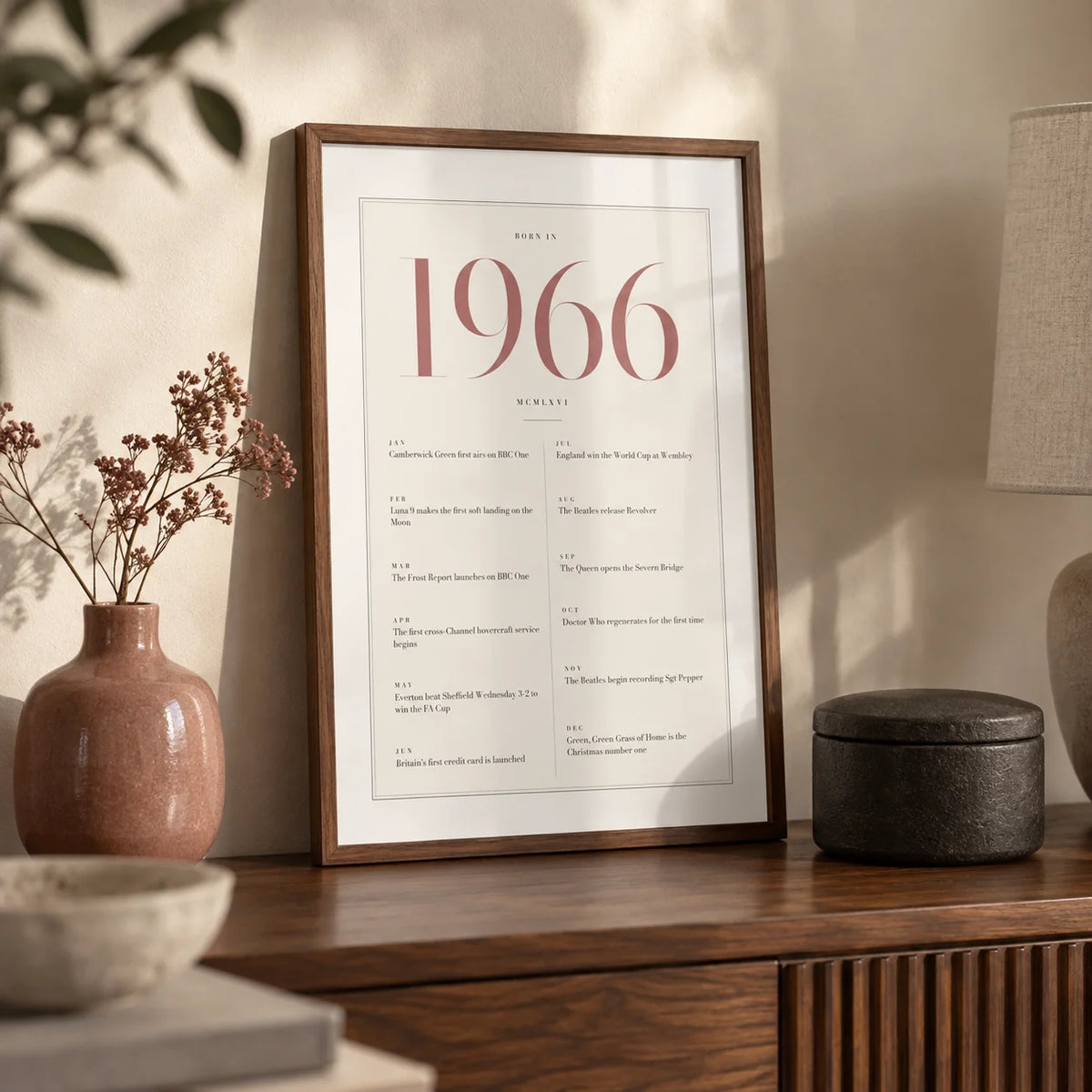 1966 Pink Birthday Print, a small A4 framed print leaning on a walnut side table in a hallway