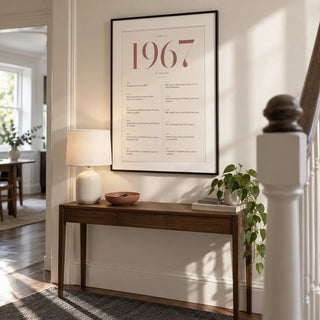1967 Pink Birthday Print, framed on the wall of a bright contemporary hallway in a UK townhouse with a warm white wall and simple painted stair balustrade