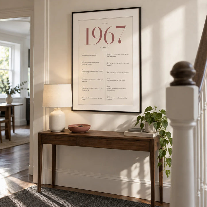 1967 Pink Birthday Print, framed on the wall of a bright contemporary hallway in a UK townhouse with a warm white wall and simple painted stair balustrade