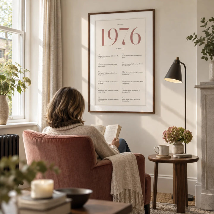 1976 Pink Birthday Print, framed on the wall of a quiet reading corner beside a tall window in a UK sitting room with an ivory wall in a living room