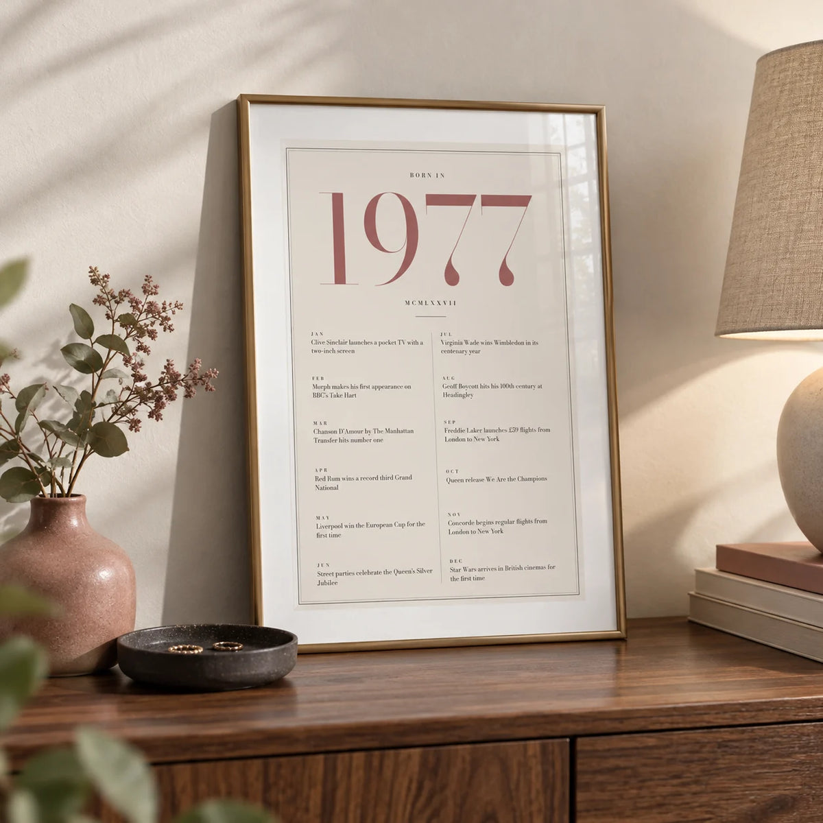 1977 Pink Birthday Print, a small A4 framed print leaning on a walnut sideboard in a living room