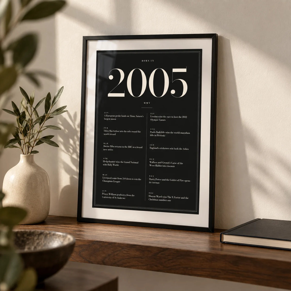 2005 Black Birthday Print, a small A4 framed print leaning on a walnut shelf in a living room