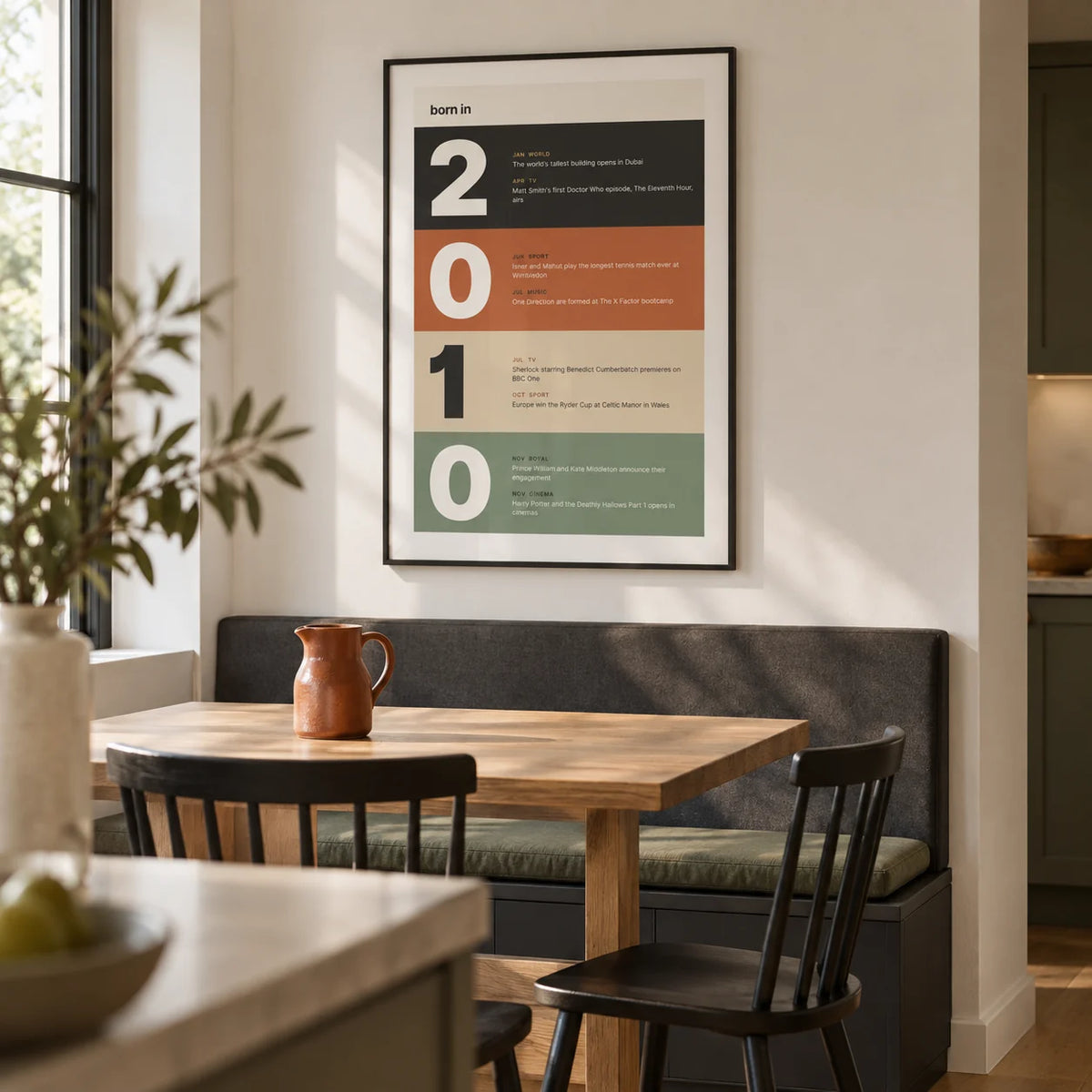 2010 Typography Print, framed on the wall of a compact modern dining nook in a UK family kitchen with an off-white wall and plain oak floor