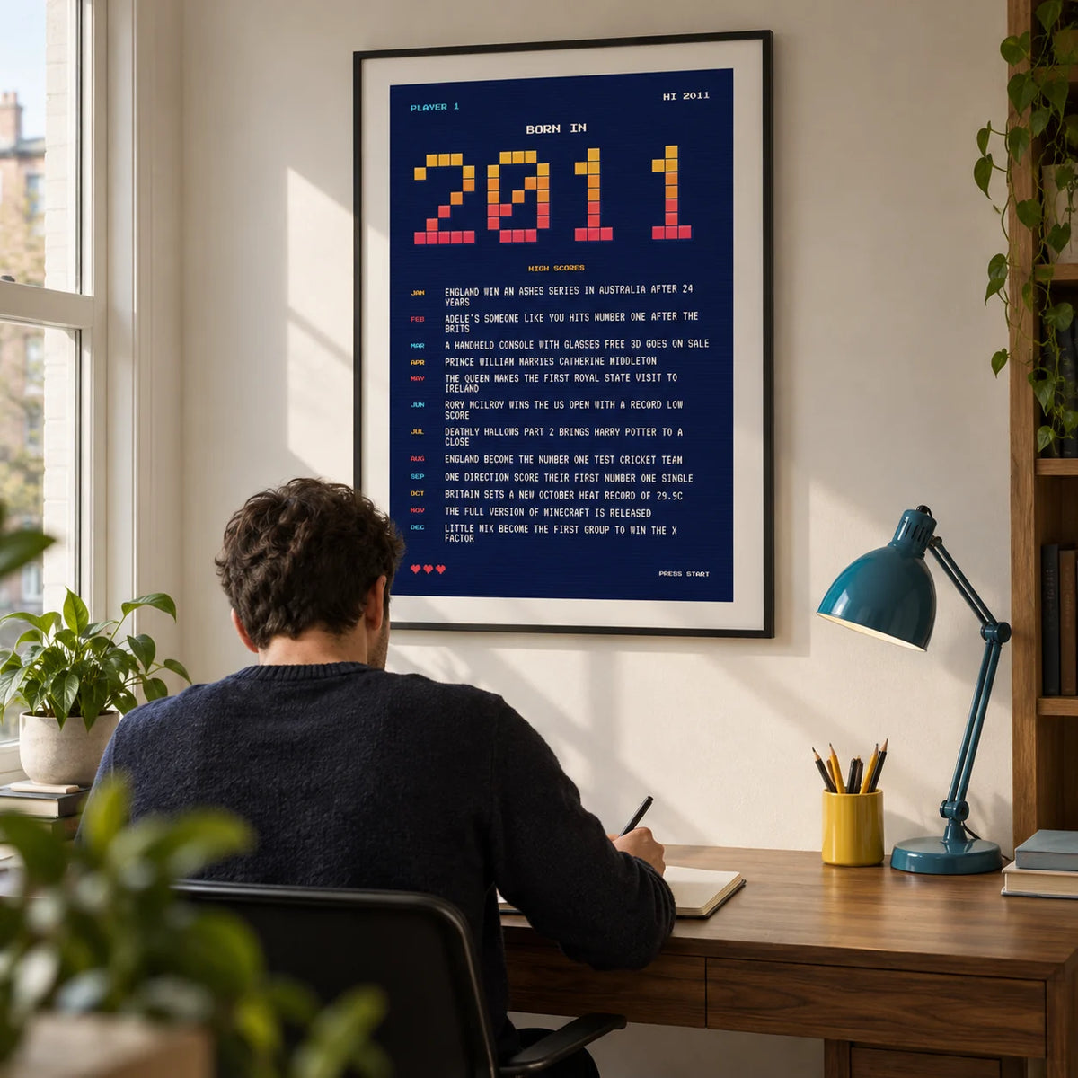 2011 Pixel Art Print, framed on the wall of a compact modern home study in a UK flat with an off-white wall and a walnut desk