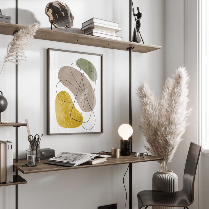 Geometric Abstract Poster print on a wall with natural shapes in muted green, yellow and grey above a desk with an open book