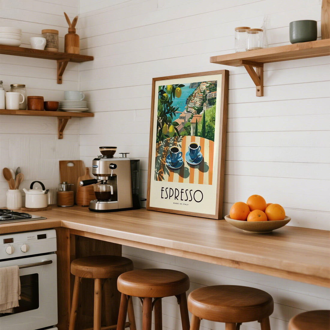 Espresso print from an Italian coastal poster series above a wooden kitchen counter with open shelves and bar stools