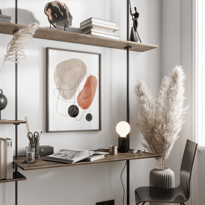 Abstract Shapes Art Print on a wall above a desk with books and pampas grass in a vase