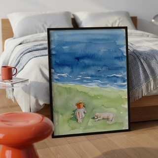 Coastal watercolor print showing layered ocean bands, grassy slope, and a person reading beside a dog