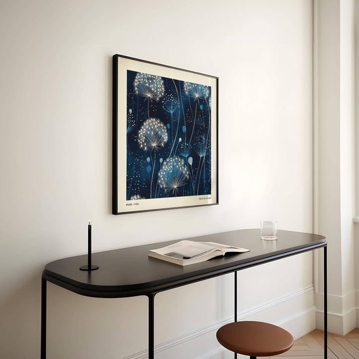 Blue art work of dandelion seed heads in white and blue hung above a black console table with a candle and an open book