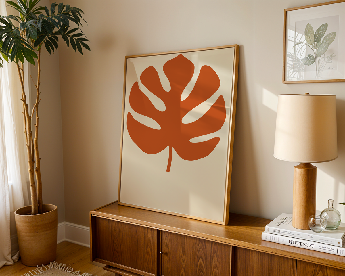 Monstera print in burnt orange leaning on a wooden sideboard in a warm living room