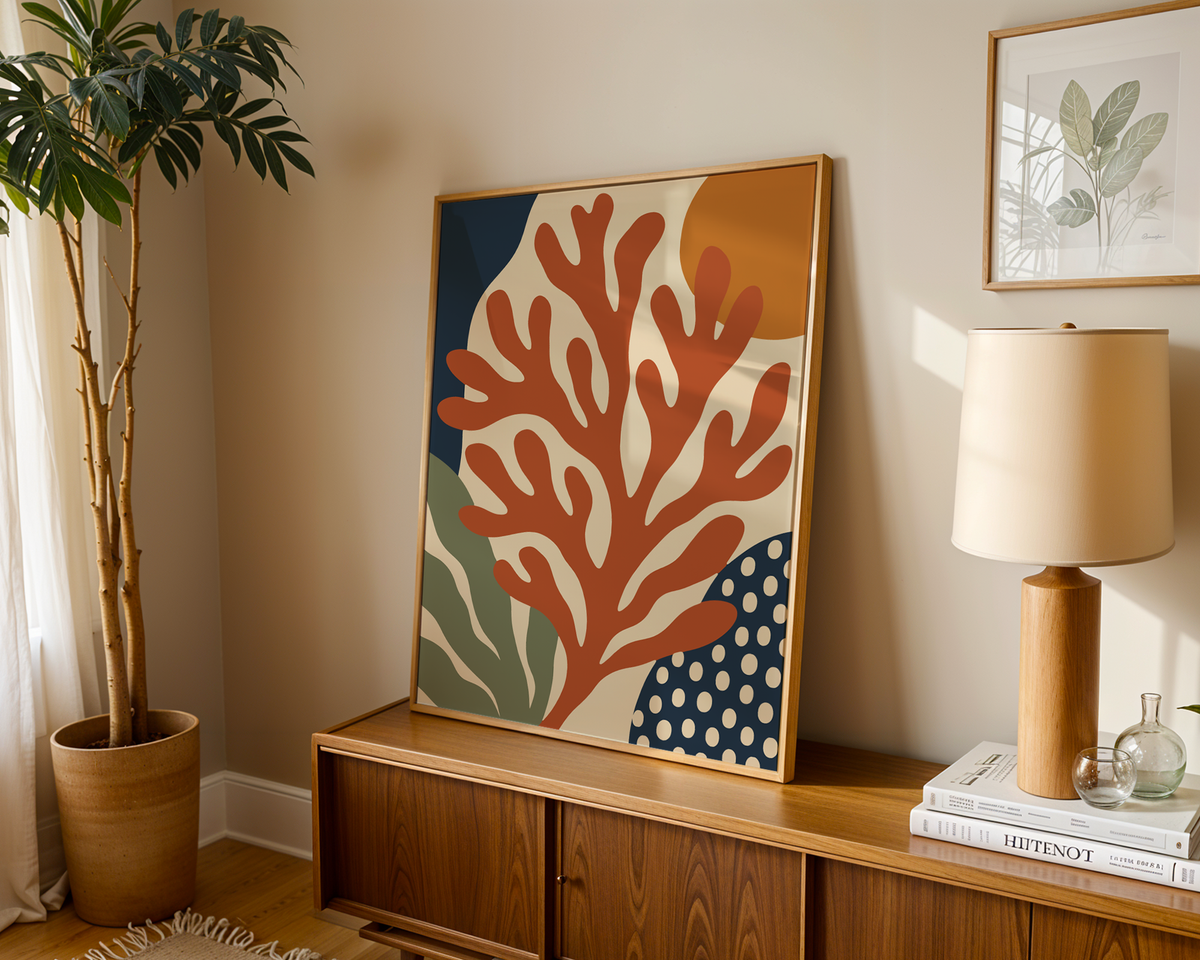 Coral wall art with an orange sun leaning on a wooden sideboard in a warm living room