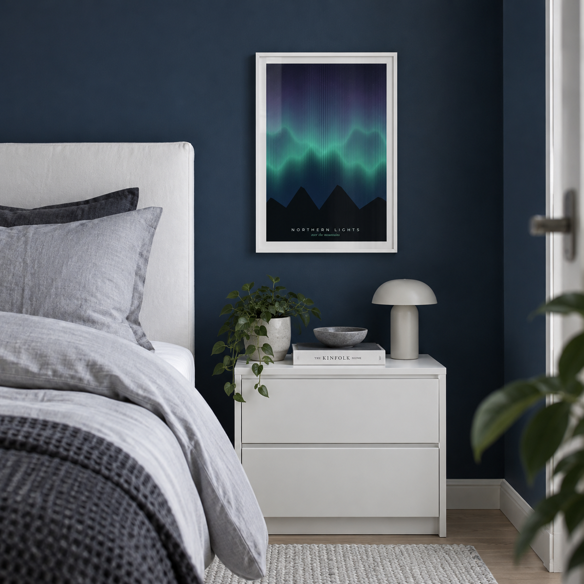 Green aurora over mountains print beside a bed against a navy wall