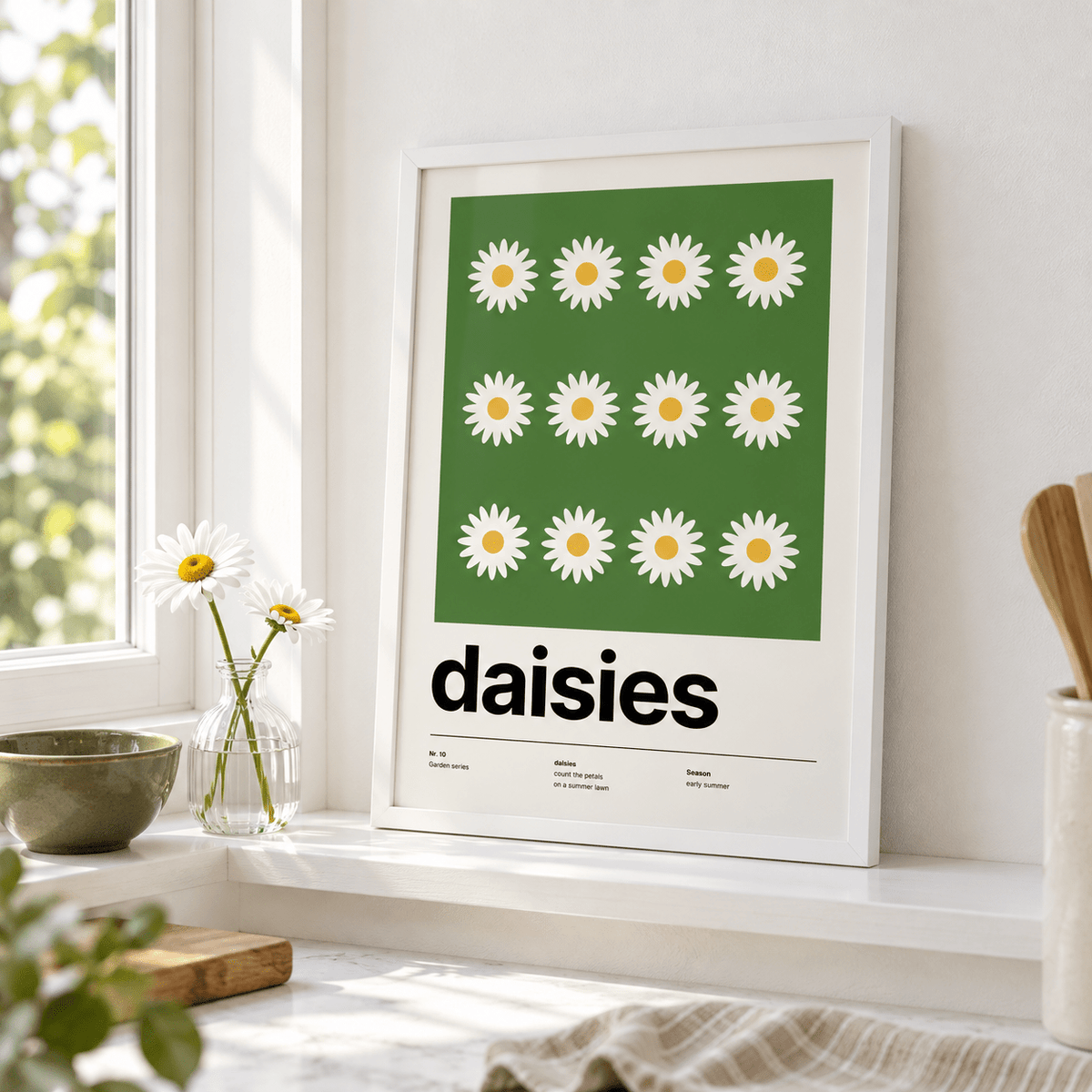 Twelve white daisies on a green lawn leaning on a ledge in a bright kitchen