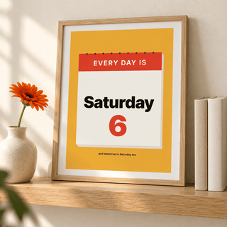 Mustard Saturday calendar print leaning on a shelf beside books and plants
