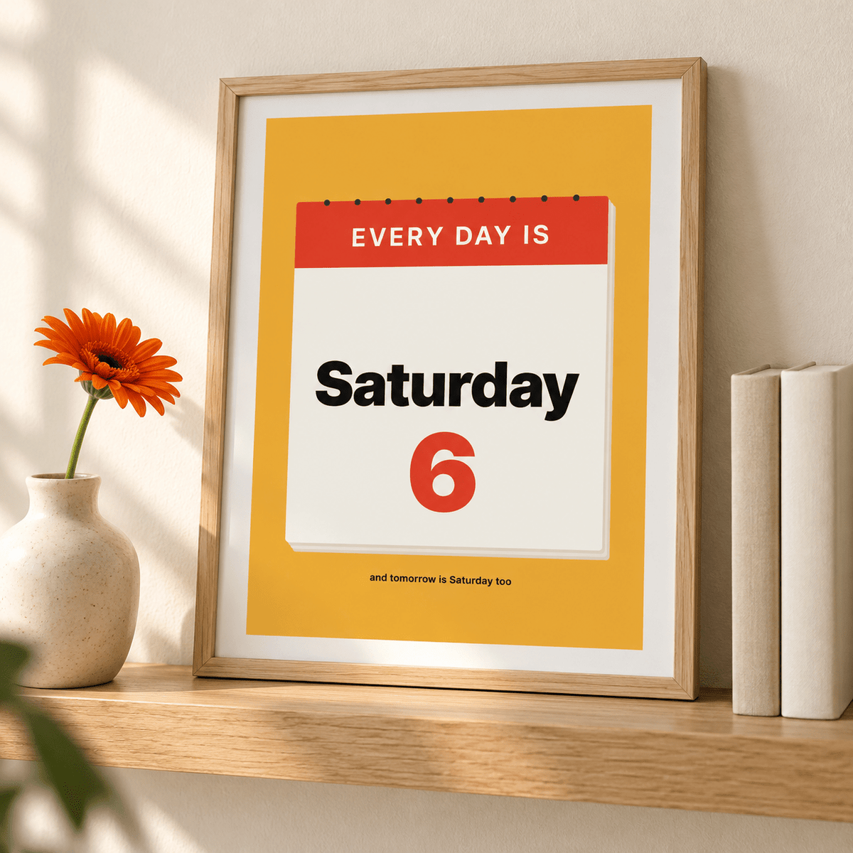 Mustard Saturday calendar print leaning on a shelf beside books and plants