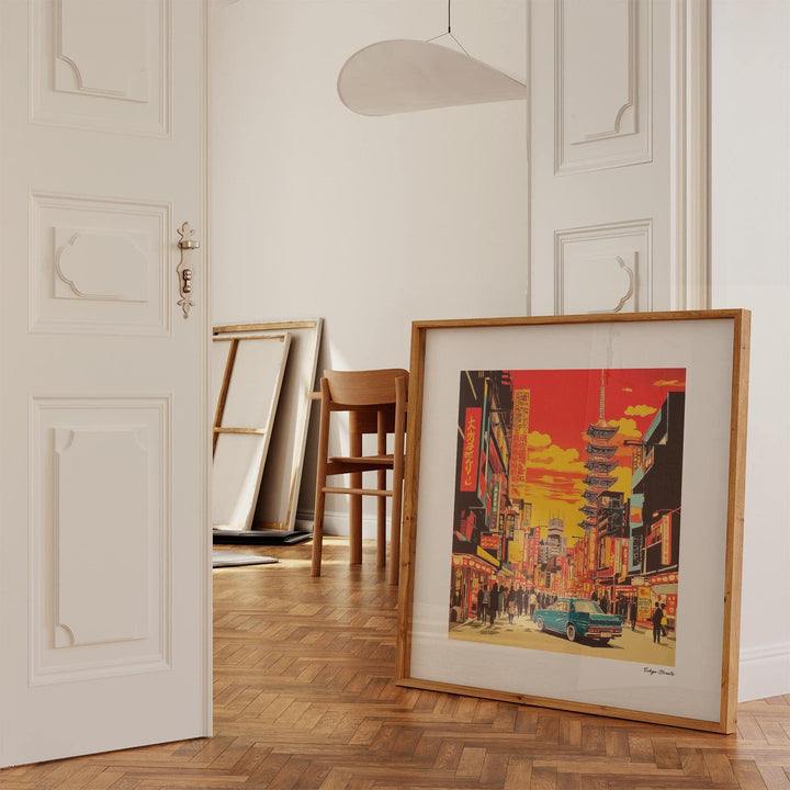 Print leaning on a wooden floor with a retro Tokyo street scene in warm orange and yellow hues and a wooden chair nearby