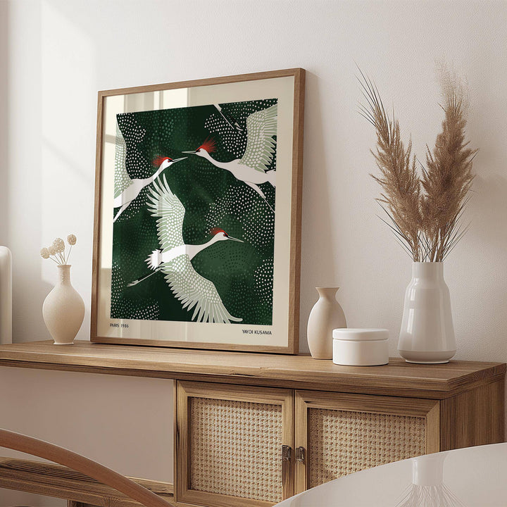 Print leaning on a shelf with white cranes on a deep green background and pale wood furniture