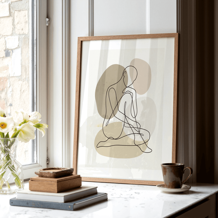 Print leaning on a surface of a seated person outline in black line art with beige shapes and a coffee cup nearby