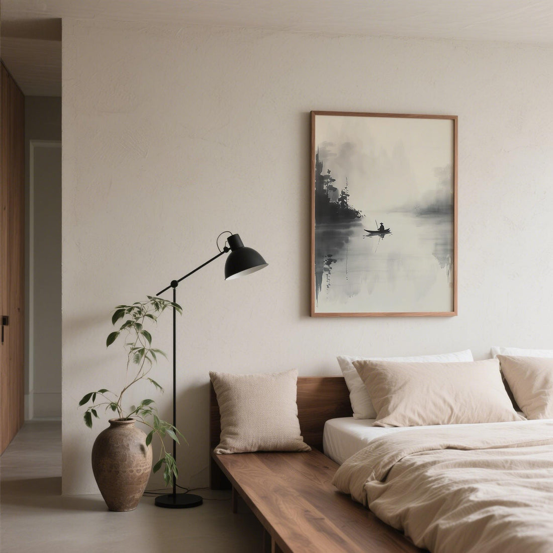 Misty ink landscape print of a small boat on a still lake, hung above a low wooden bed with linen bedding and a black floor lamp