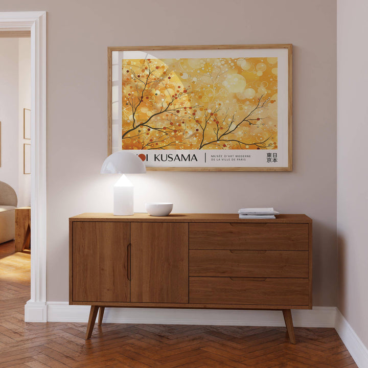 Landscape poster of branches with berries in warm yellow and orange hues above a wooden sideboard