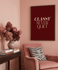 Serif quote print reading “CLASSY NEVER QUIET” in beige uppercase against deep crimson background