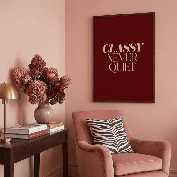 Serif quote print reading “CLASSY NEVER QUIET” in beige uppercase against deep crimson background