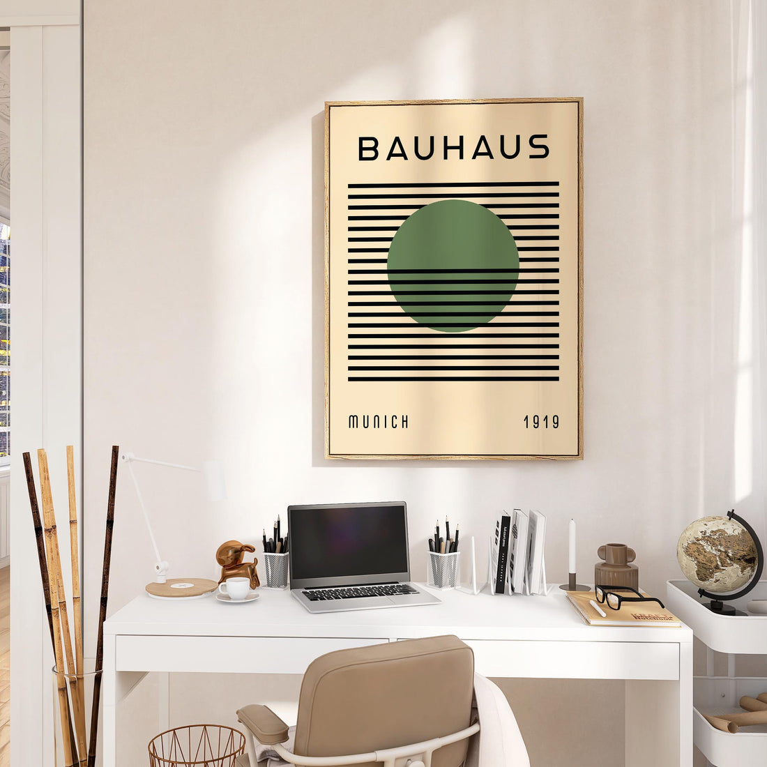 Cream Bauhaus print with a green circle and black stripes hanging above a white desk with a laptop and lamp
