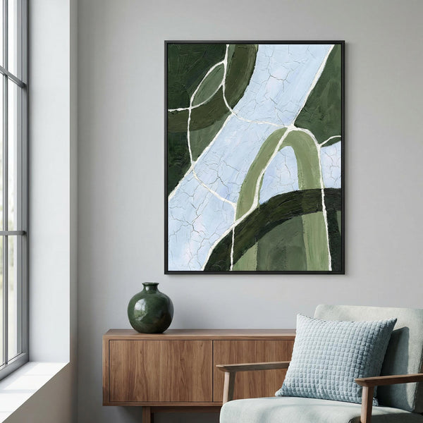 Abstract art piece on a wall above a wooden side table with a green vase and a light blue pillow on a chair.