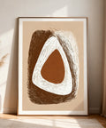 Abstract art print with brown and white shapes in a gold frame on a beige wall.