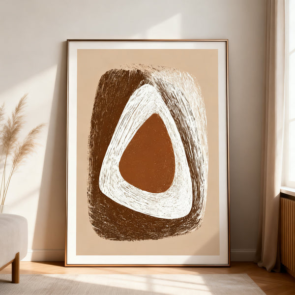 Abstract art print with brown and white shapes in a gold frame on a beige wall.