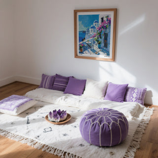 Room with a bed covered in white bedding and purple pillows, a purple pouf, and a Santorini Wall Art framed on the wall.