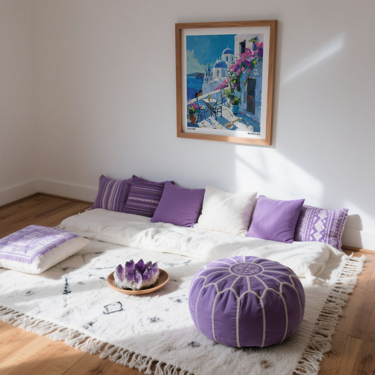 Room with a bed covered in white bedding and purple pillows, a purple pouf, and a Santorini Wall Art framed on the wall.