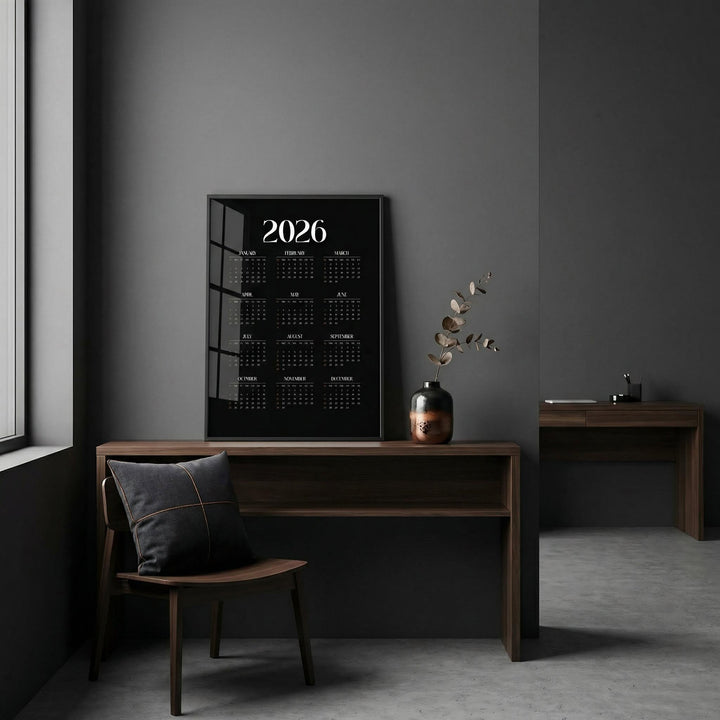 Modern Calendar Print leaning on a desk with a dark wall and a vase with dried leaves