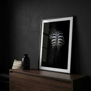 Framed black and white zebra print on a dark wall with a wooden cabinet.