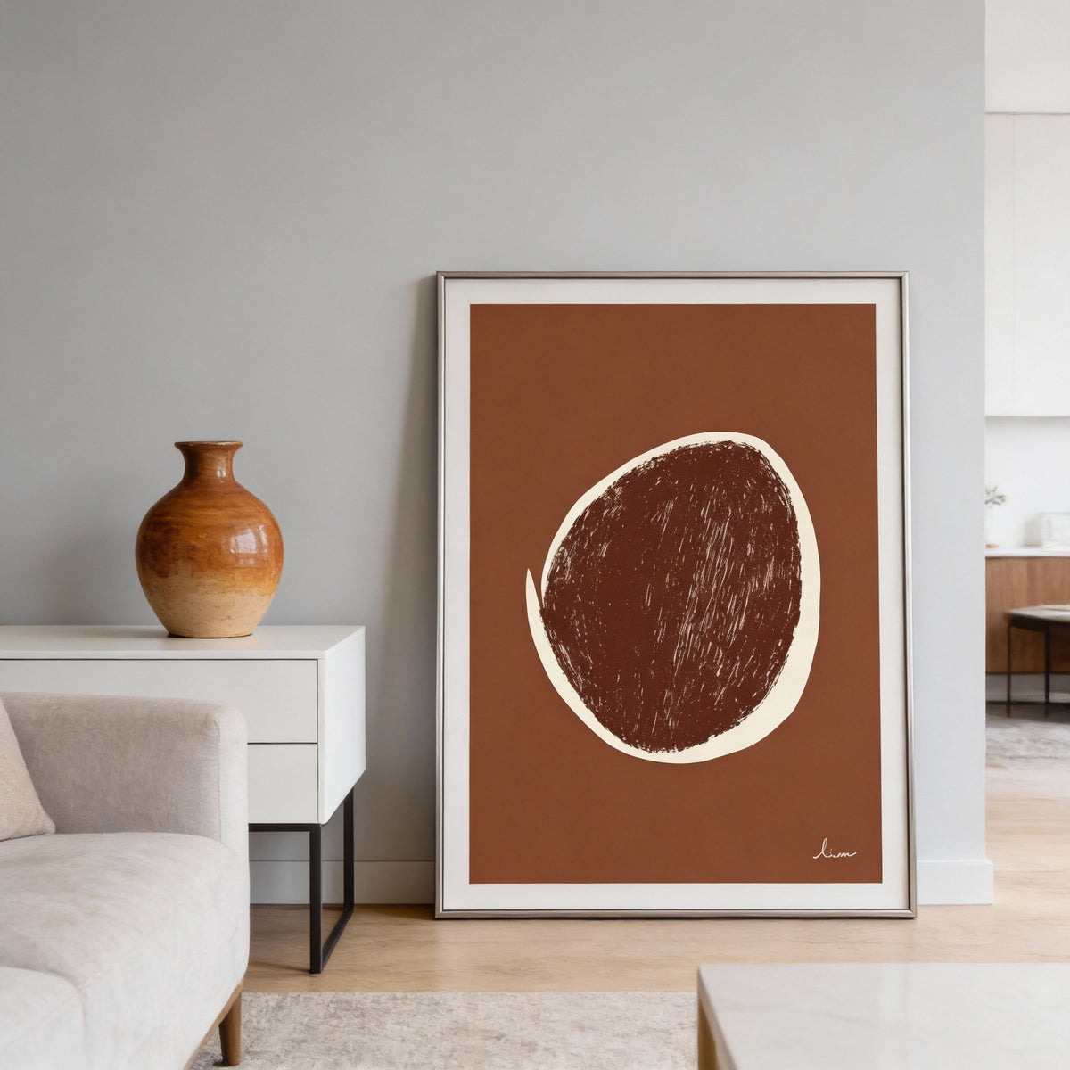 Framed abstract art print on a wall with a vase and sofa in the background