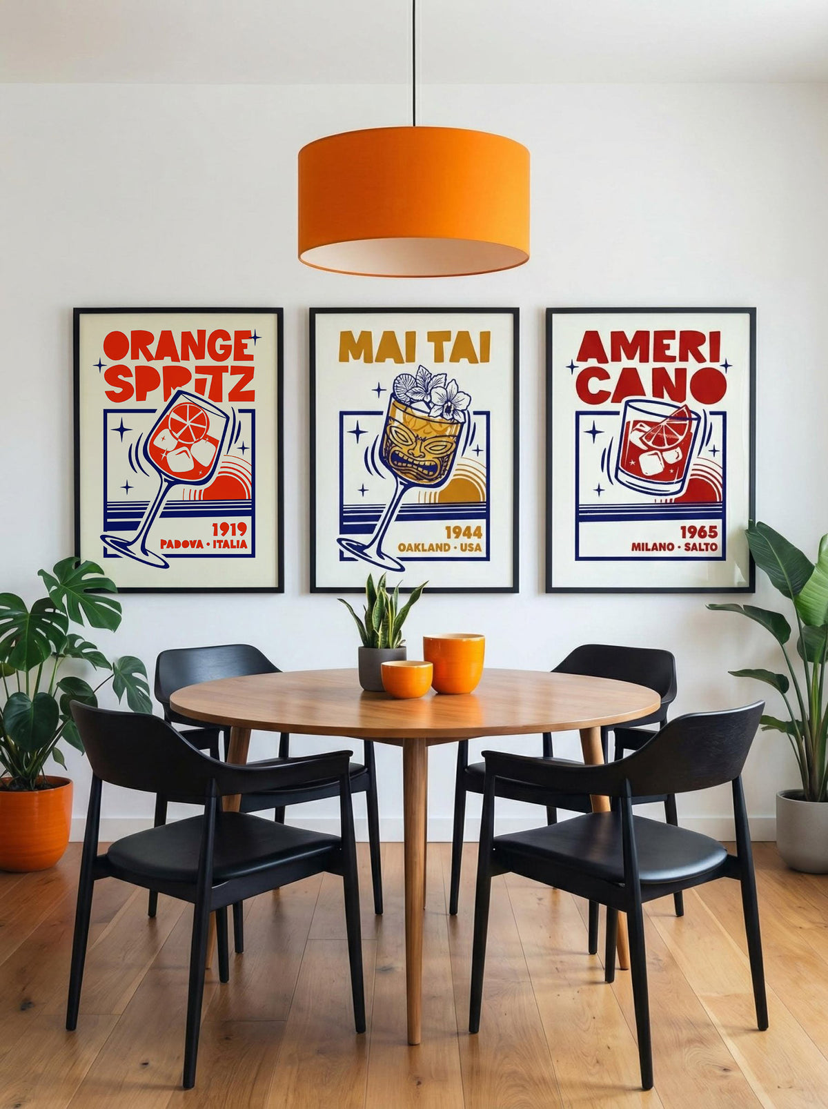 A styled dining room scene with a round wooden table, four black chairs, an orange pendant light, and three framed retro-style posters on the wall reading 'Orange Spitz', 'Mai Tai', and 'Ameri Cano'.